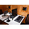 Two desks in a wooden house. Laptops, monitors and desk lamps are on the desks. Windows in the background.
