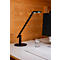 A black desk lamp illuminates a desk with a glass of water, a keyboard, and a computer screen.