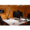 Desk in wood-paneled room: two black lamps, monitors, keyboard, mouse, headphones, glass of water. A picture on the wall.
