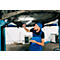 Mechanic in blue overalls inspects the undercarriage of a car. He holds a flashlight and a folder.