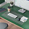 Bureau met groene ondergrond, toetsenbord, muis, notitieblok, koffiebeker, plant en monitor.