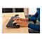 Hände einer Person, die eine schwarze Tastatur auf einem Holzschreibtisch bedient. Die Person trägt einen blauen Pullover und Ringe.