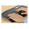Gros plan d'une personne tapant sur un clavier Logitech sombre ; mains sur les touches, manche bleu en arrière-plan.