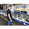 Een man in een zwart t-shirt staat aan een lopende band in een fabriek en controleert machines.