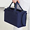 Eine dunkelblaue Filztasche wird per Schlaufe flexibel am Griff eines schwarzen Rollkoffers befestigt.