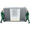 Two workers assembling a metal cabin. They wear green overalls and hold the walls.