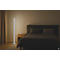 Schlafzimmer mit Stehlampe und Bett. Die Lampe leuchtet hell, das Bett ist dunkel. Auf dem Nachttisch steht ein Glas.