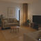 Ein Wohnzimmer mit Couch, Kaffeetisch, Fernseher, Pflanzen und einer Stehlampe. Die Beleuchtung ist sanft und warm.