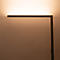 Eine minimalistische, dunkle LED-Stehleuchte wirft warmes, indirektes Licht an die Wand.
