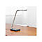 Modern, silver desk lamp on a brown wooden surface. The lamp head is rectangular. In the background a white room.
