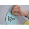 A hand inserts a yellow pushpin into a blue paper circle that says "Björn."