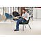 Ein Mann in Jeans und Hemd sitzt in einem grünen Sessel und liest. Im Hintergrund weitere Stühle und ein Fenster.