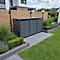 Trois poubelles grises sont dans un jardin devant une clôture en bois, entourées de plantes et de pelouse.