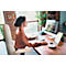 Une femme est assise à un bureau et travaille sur un ordinateur. Sur le bureau, il y a une tasse de café, un bloc-notes et un stylo.