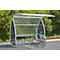 Bicycle stands under a transparent shelter with a metal frame. Trees in the background.