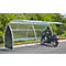Motorcycle under a metal shelter on asphalt. Green bushes in the background.