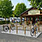 Ein hölzerner Fahrradständer vor dem Rezeptionsgebäude eines Campingplatzes mit Wohnmobilen im Hintergrund.