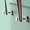 Close-up of wall storage details. Brown leather straps hang on silver pins in a light green wall.