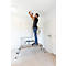 Een man staat op een ladder en repareert een plafondlamp. Hij draagt een spijkerbroek, een zwart t-shirt, sneakers en gebruikt rode tangen.
