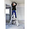 Een man in blauwe werkkleding staat op een ladder en monteert een lamp aan het plafond.