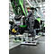 Un homme travaille sur un tracteur vert, debout sur un escabeau. Dans un hall d'usine, capot ouvert.