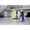 A man pushing a yellow FlexxTower scaffolding cart on wheels in a warehouse. A staircase in the background.