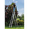 Een man staat op een zilveren ladder en snoeit een heg. De ladder staat in de tuin onder een blauwe hemel.