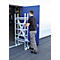 A man pushes a metal scaffolding through a blue door. Scaffolding with rollers, gray trousers and black shirt.