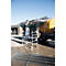 A man sprays a tanker with a hose attachment and a lift. A farm in the background.