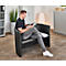 Ein Mann sitzt in einem schwarzen Ledersessel und liest eine Zeitschrift. Er trägt Jeans, ein schwarzes T-Shirt und weisse Schuhe.