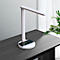 Witte bureaulamp met geïntegreerd oplaadstation met een smartphone erop. De lamp staat op een donker bureau.
