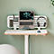 Bureau debout avec ordinateur portable, casque et fournitures de bureau contre un mur vert clair.