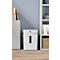 White paper shredder with viewing window, standing on light wooden floor in front of light blue wall. Books to the left, shelf with books to the right.