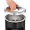 Hand lifting a shiny lid off a black trash can.