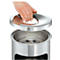 A hand lifts the lid of a stainless steel trash can.