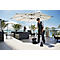 Serveuse balayant la terrasse sous un parasol, vue sur la mer. Une autre personne se tient au fond.
