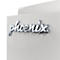 Nahaufnahme des verchromten Phoenix-Logos in Schreibschrift auf einer hellgrauen Oberfläche.
