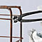 Pince noire liant du fil autour d'une armature en acier. Gants tenant la pince. Le fond est clair.