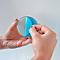 Des mains tiennent un disque rond et transparent, en train de décoller un film protecteur bleu. Le fond est blanc.