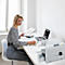 Une femme est assise à un bureau, tenant un presse-papiers et écrivant. Imprimante et ordinateur portable sur la table.