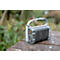 Grey waterproof speaker with a handle, in the rain on a wooden surface.