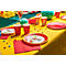 Table dressée de manière festive avec des assiettes, des gobelets, des serviettes et des bonbons sur une nappe jaune.
