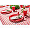 Une table dressée de façon festive avec une nappe à carreaux rouges et blancs. Assiettes, gobelets et serviettes rouges avec des brins d'herbes.