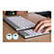 Hände nutzen eine ergonomische, getrennte Tastatur und ein separates Ziffernfeld auf einem Holztisch.