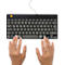 Schwarze Tastatur mit grauen Tasten. Darunter sind zwei Hände in Schreibposition.