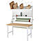 Packstation mit Tisch, Packpapier, Kartons, Werkzeug und Regalen.