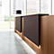 Reception desk with wood paneling and brown elements, windows in the background with a view of high-rise buildings.