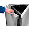 A hand holds a gray trash can lid. A black trash bag is partially visible.