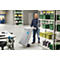 A man pulls a gray transport cart through a warehouse. Shelves with boxes are in the background.