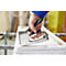 A person using a silver staple gun to attach canvas to a wooden frame.